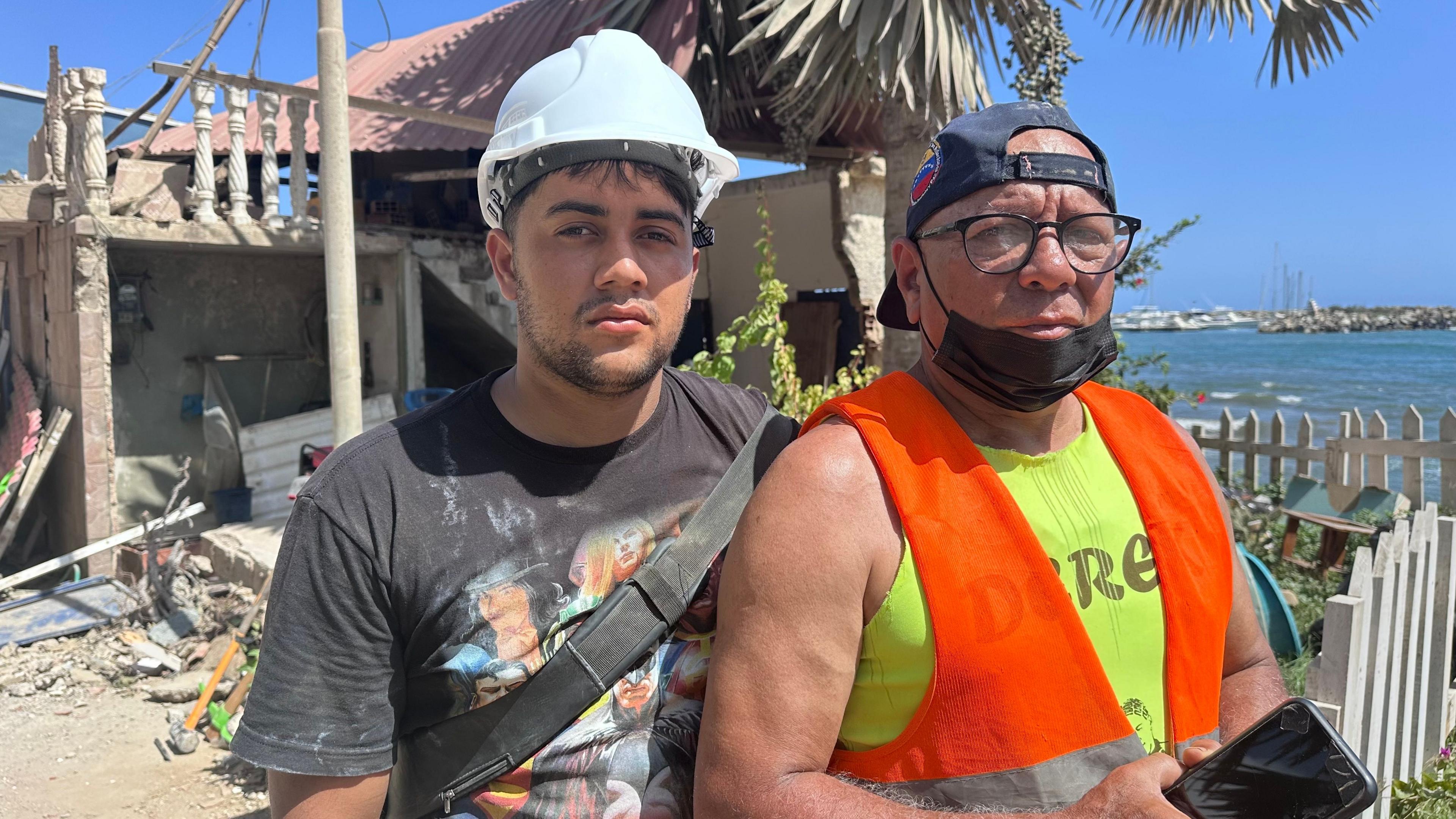 Enyer Musics and his uncle Juan Avendo stand close together in front of damaged buildings