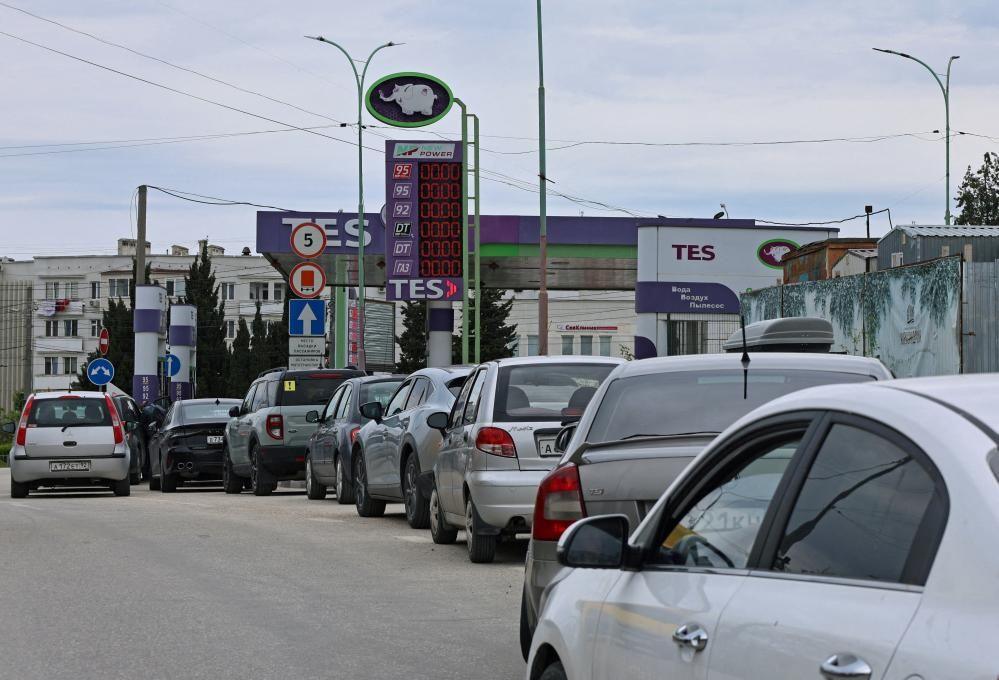 A line of silver and grey cars snaking round from a petrol station where the prices electronic display has no numbers on it.