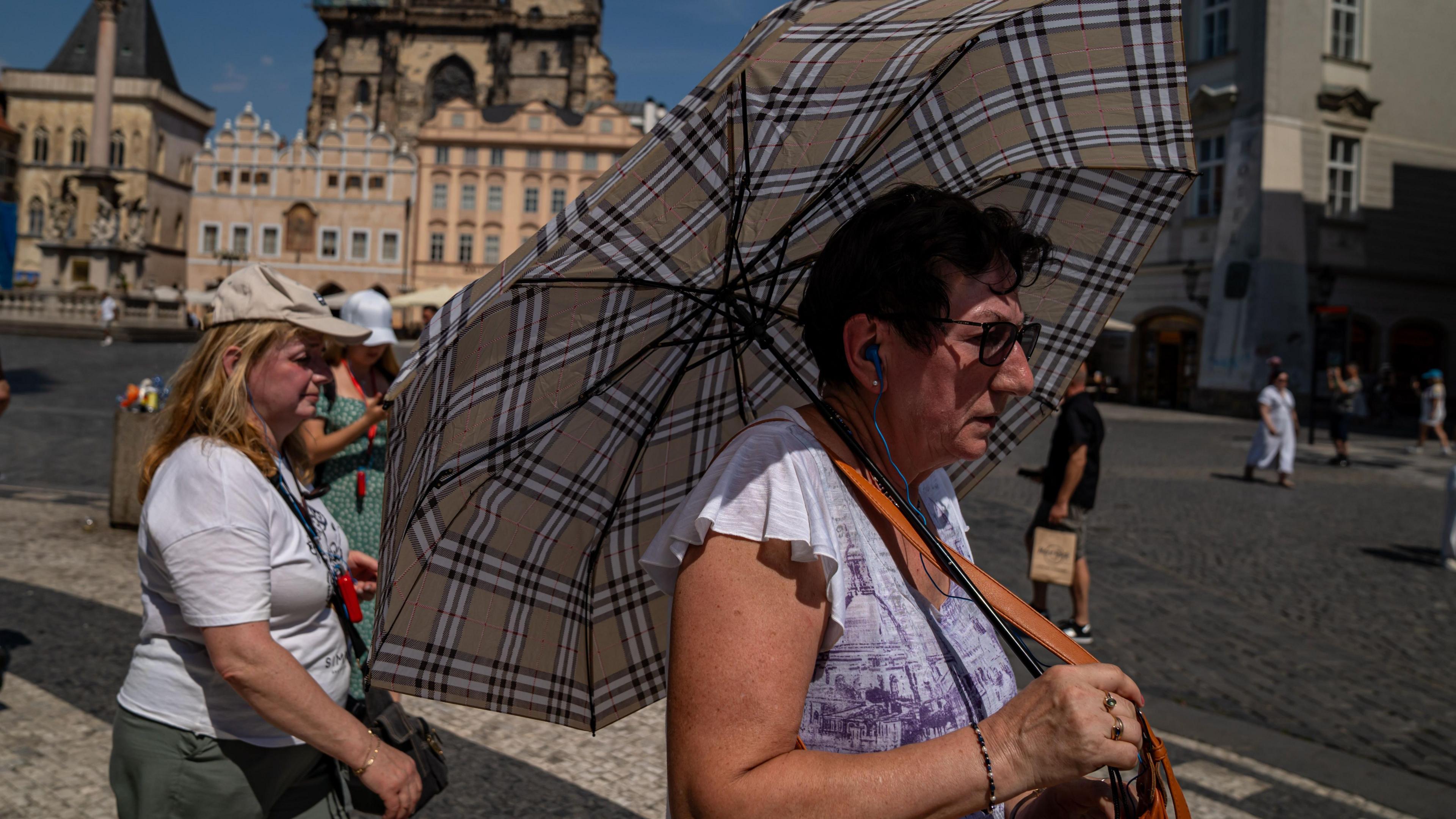 A woman with an umbrella shields herself from the sun in Prague's Old Town