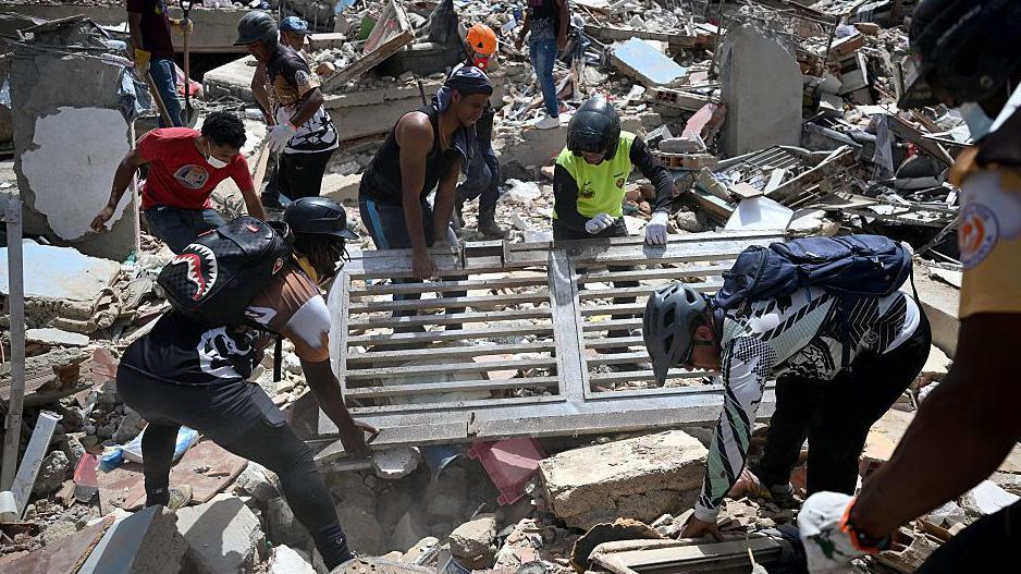 Volunteers lift a metal gate as they search through debris on the rubble of collapsed buildings in Catia La Mar.