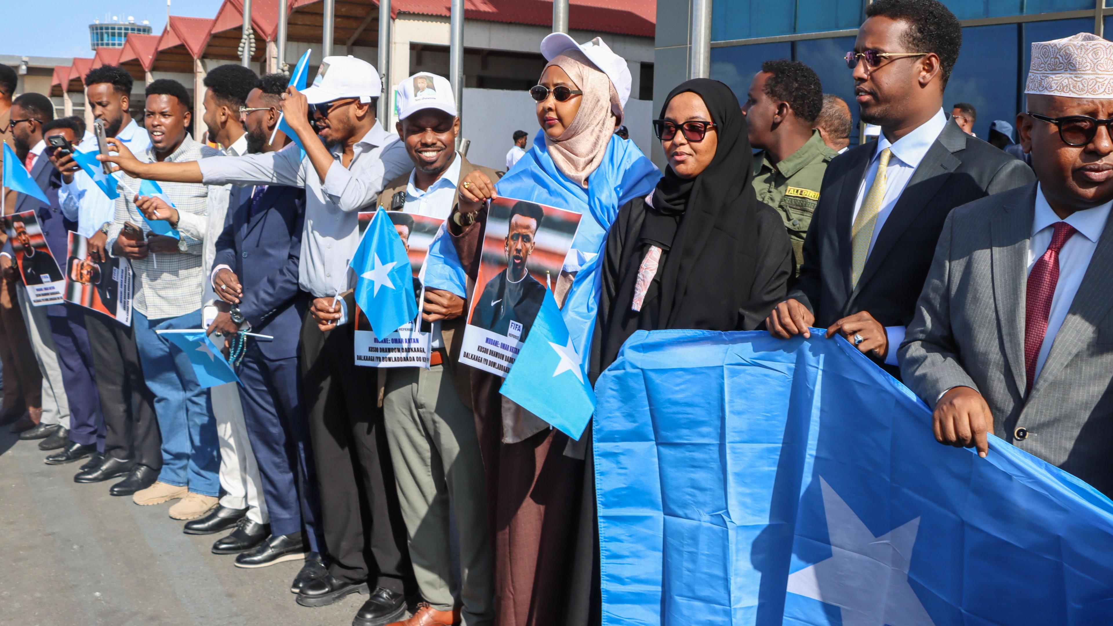 A crowd of people holding Somalia flags (pale blue with a white star) and pictures of Omar Artan