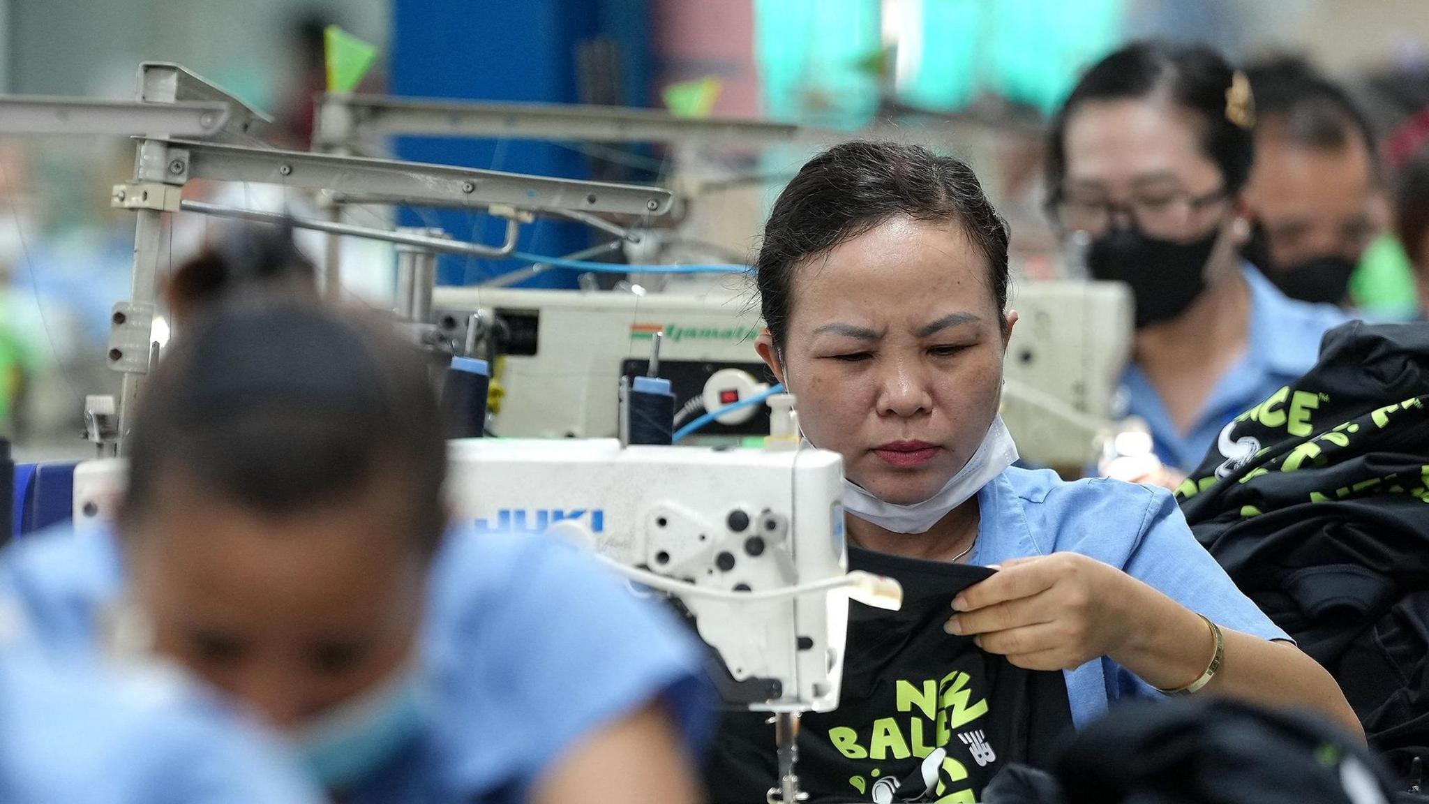 Vietnamese garment factory workers stitch apparel at a factory in Ho Chi Minh City on April 3, 2025. They are seen in a row in light blue shirts bent over white sewing machines.