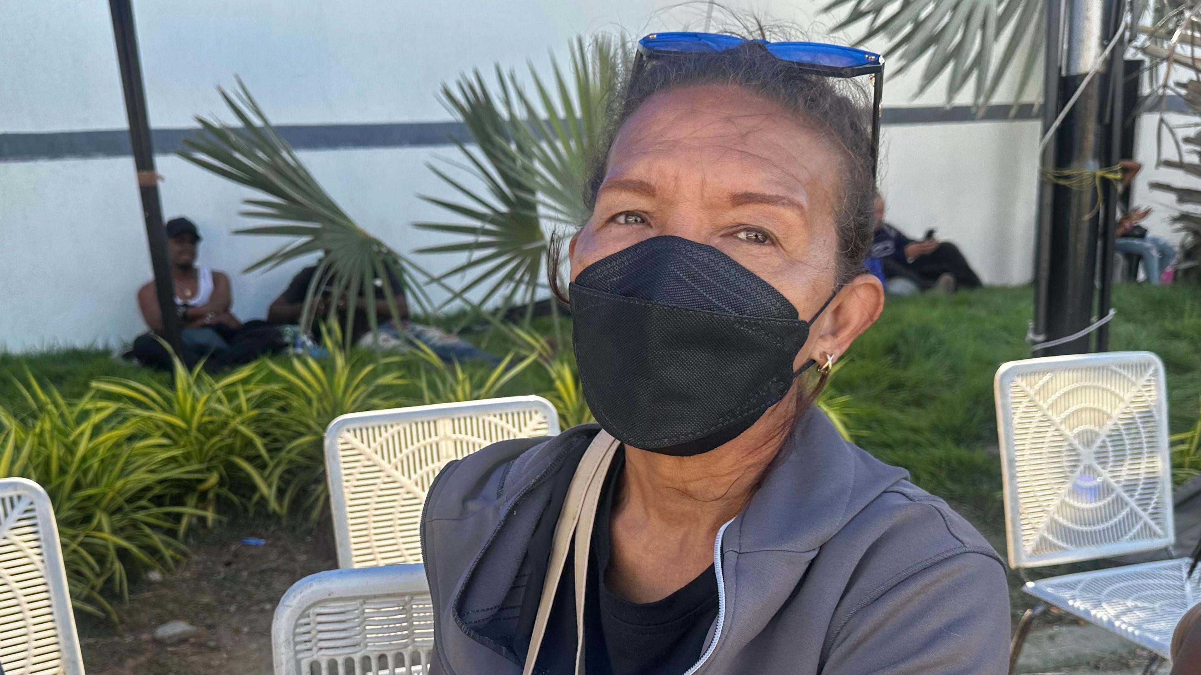 Liliana González, a 60-year-old woman sitting in a chair and wearing a black face mask.