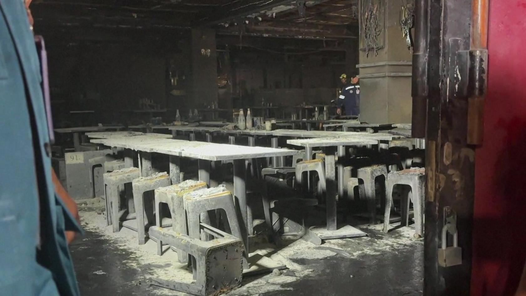 Tables and chairs are covered in ash inside the venue, which shows huge fire damage. The picture is taken through a door frame.