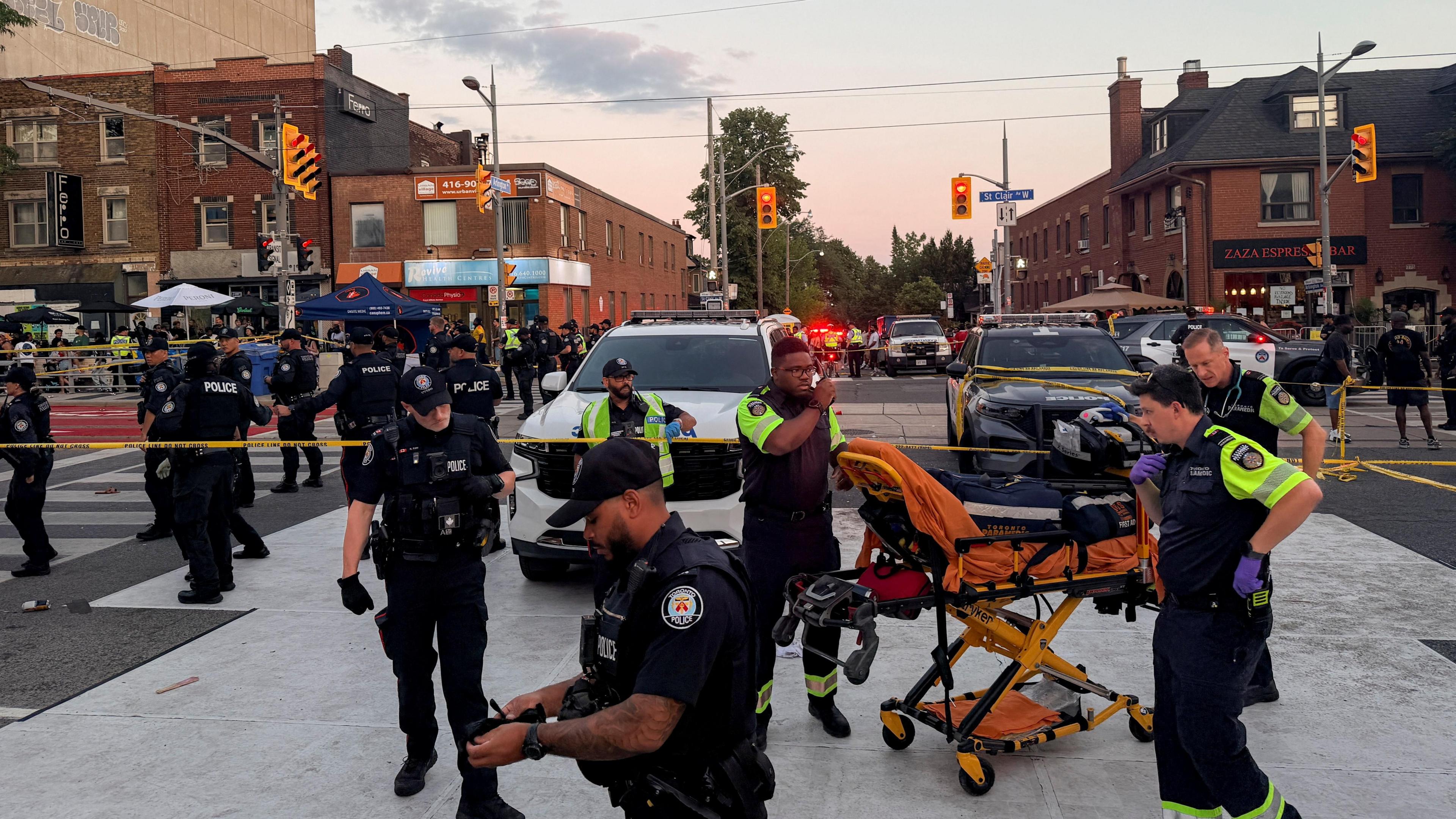 Police officers stand guard as emergency workers respond at the site of a deadly shooting at a salsa-themed street festival in Toronto.