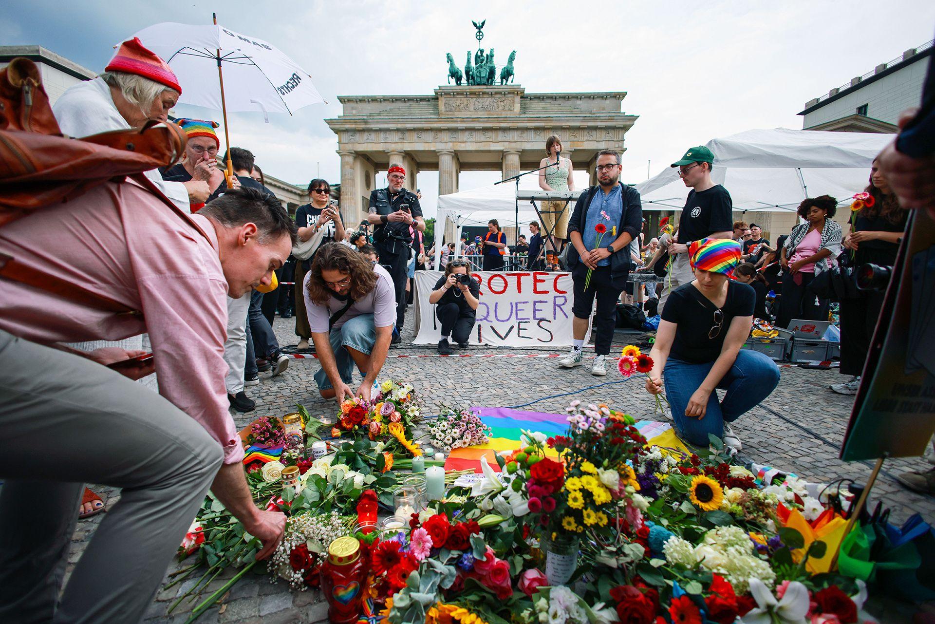 People lay flowers in front of a banner saying 'protect queer lives', with the Brandenburg Gate in the background on a cloudy day in Berlin on Sunday.
