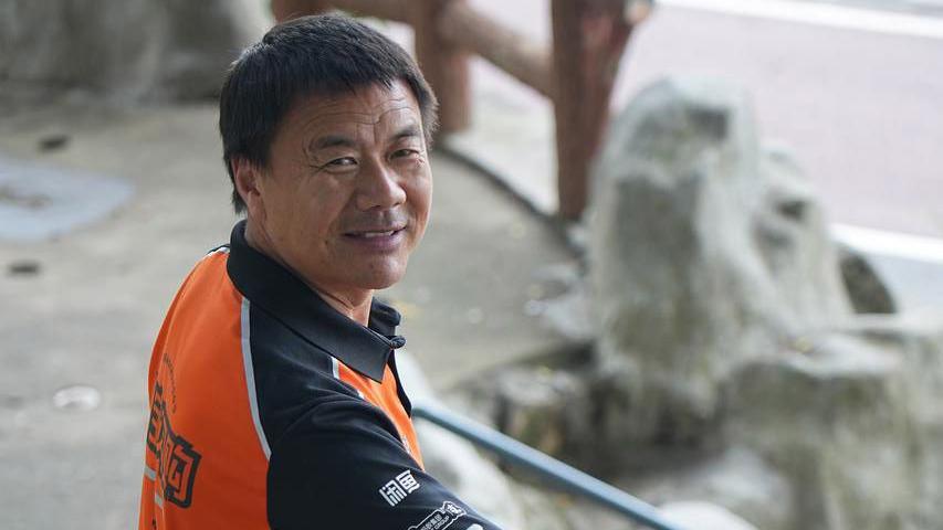 Wang Jibing in an orange polo shirt smiling at the camera