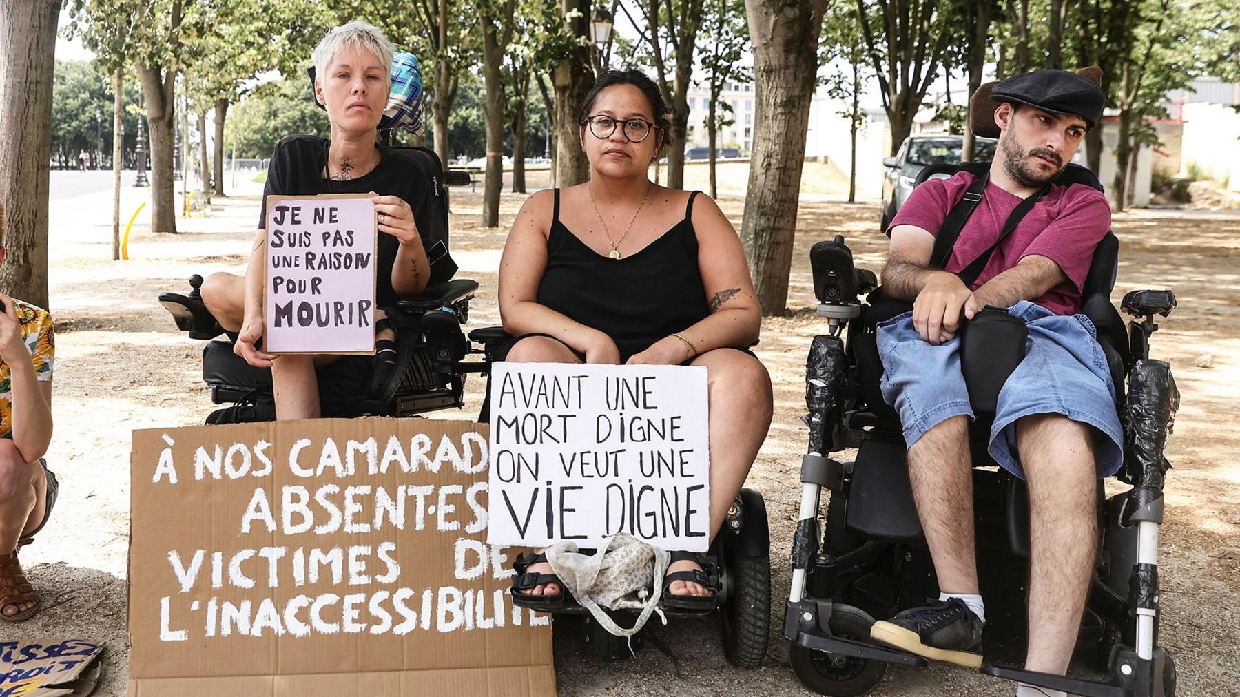 Protesters in wheelchairs hold up signs reading "I am not a reason to die " and "Before a dignified death, I want to see a dignified life"