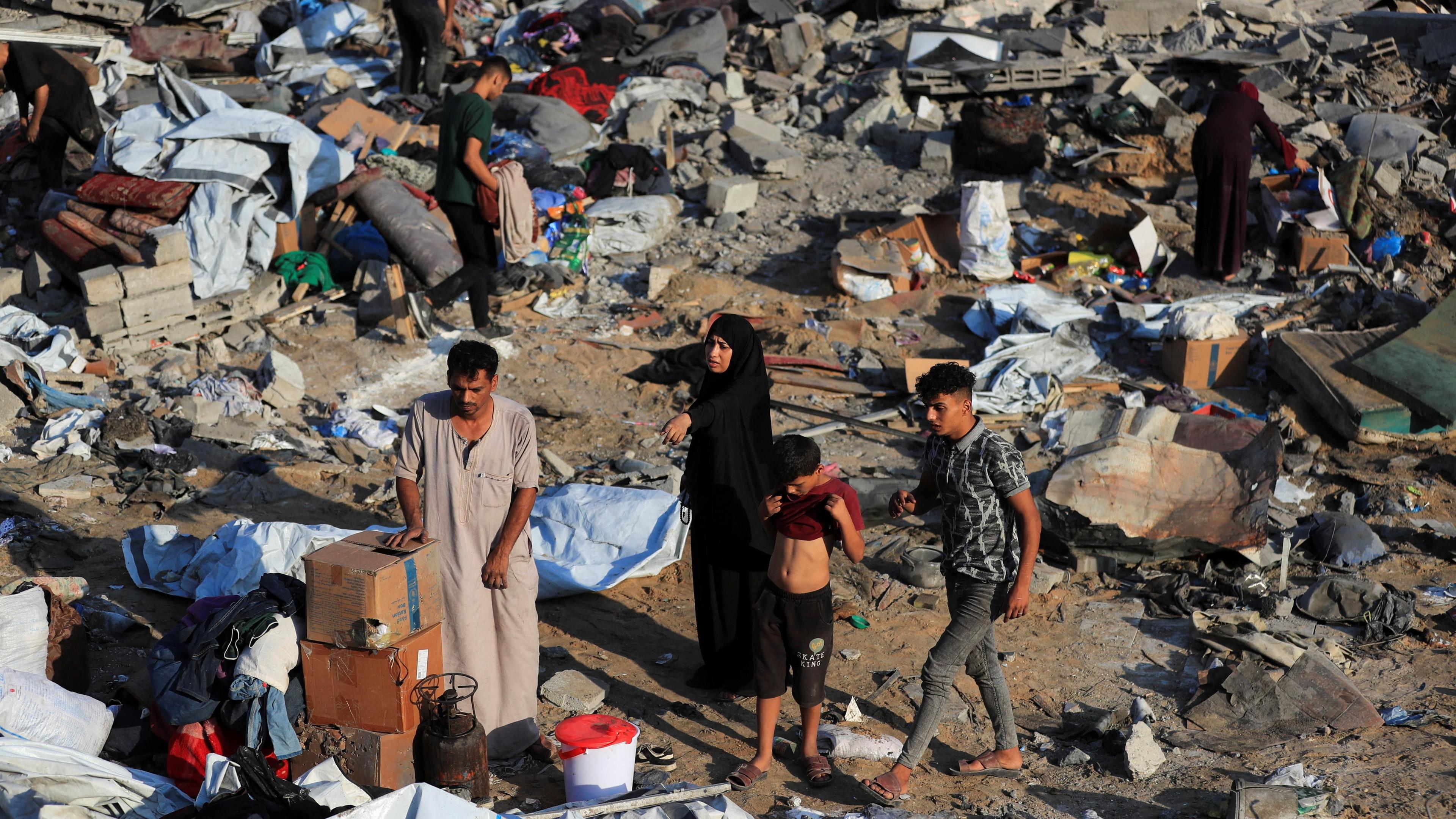 People stand in the ruins of a house, looking for belongings.