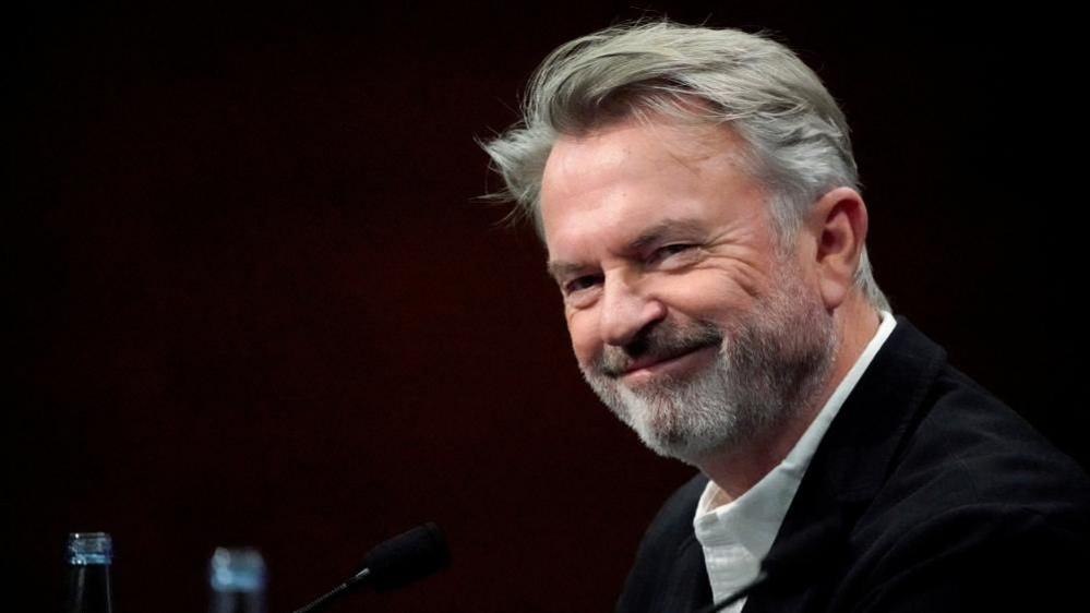 Sam Neill smiles against a black background, at the San Sebastian Film Festival in Spain in 2019