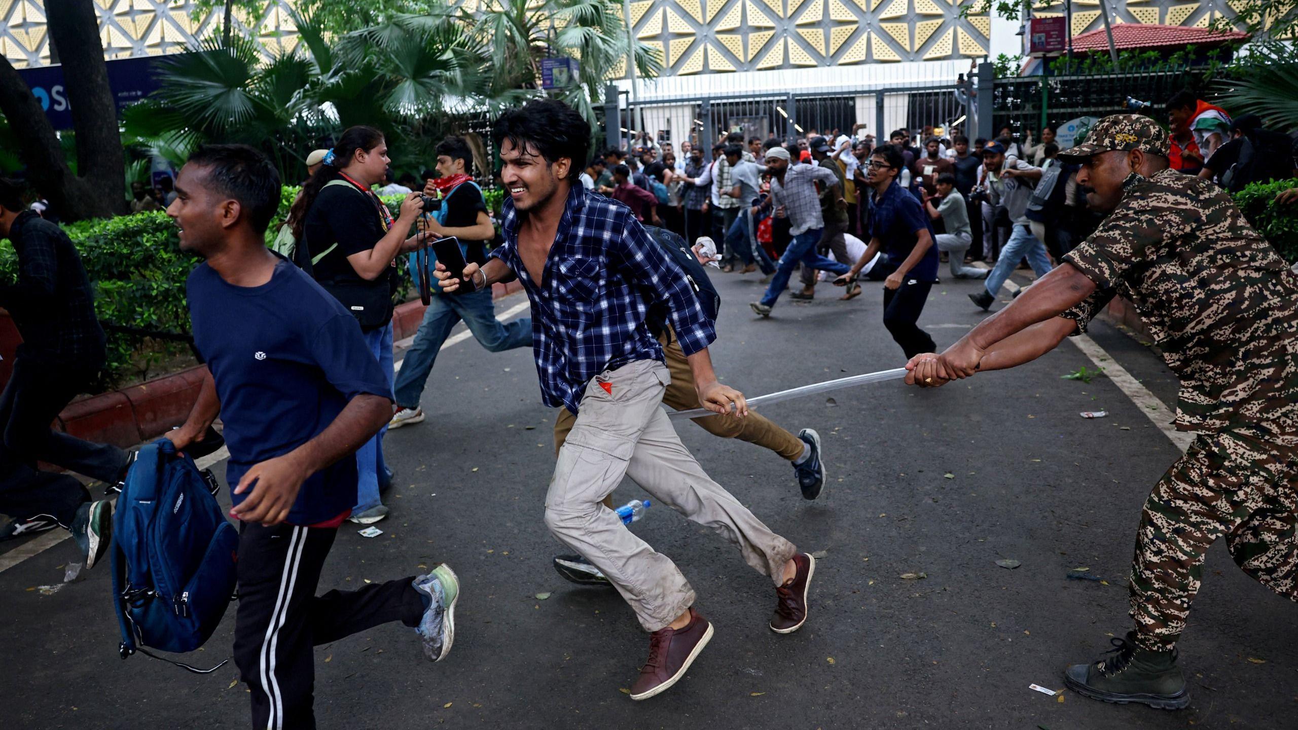 A security force personnel wields his baton against demonstrators at a protest site during a planned march by supporters of India's Cockroach Janta Party
