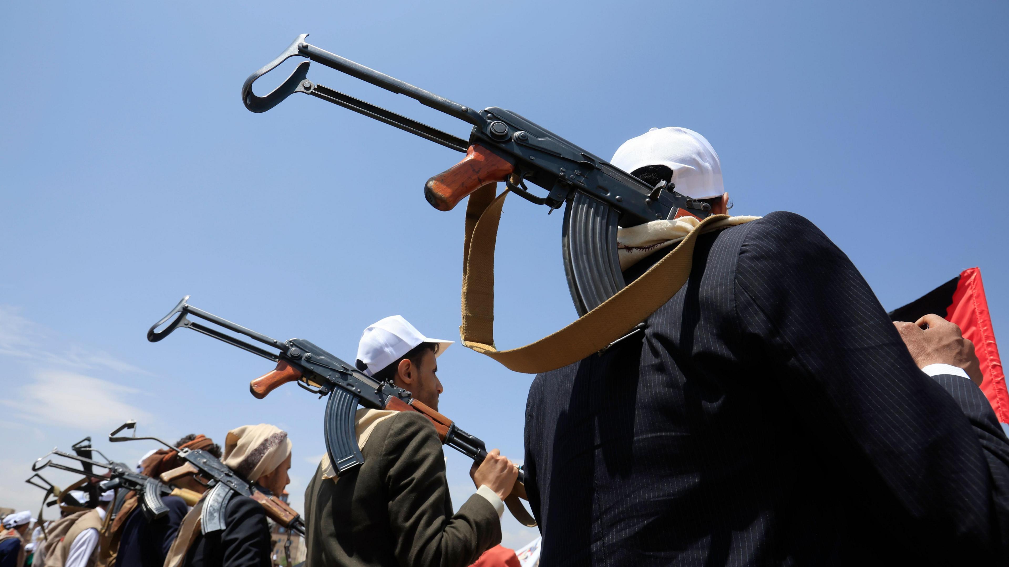 Armed students participate in a rally supporting the Houthi-imposed naval embargo against Saudi Arabia in Sana'a, Yemen, 22 July 2026. Hundreds of students gathered at Sanaa University to support the declaration. The students are seen from behind, holding assault rifles over their shoulders, wearing white baseball caps