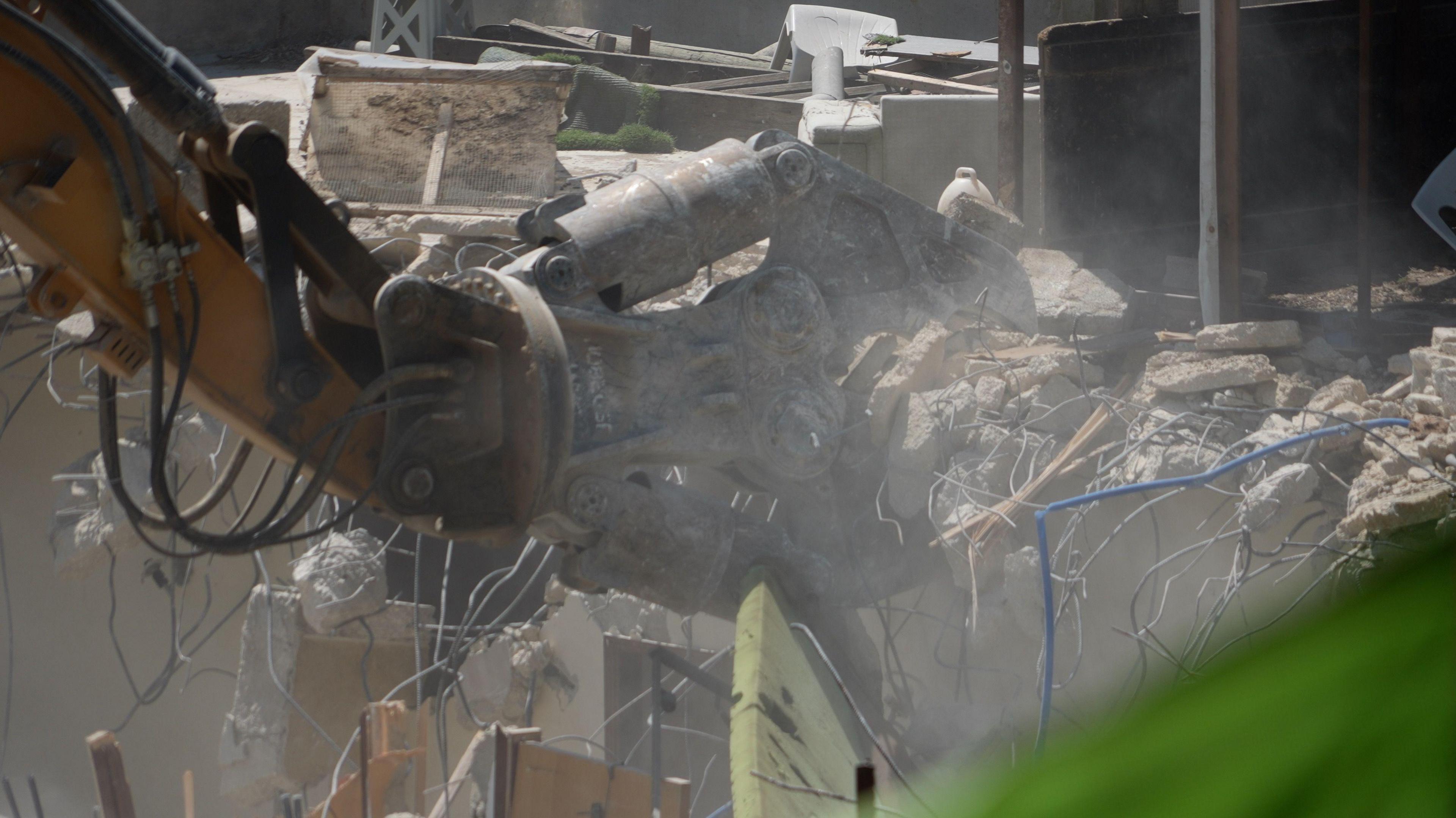 An excavator picks up rubble and wires after the demolition of a building.