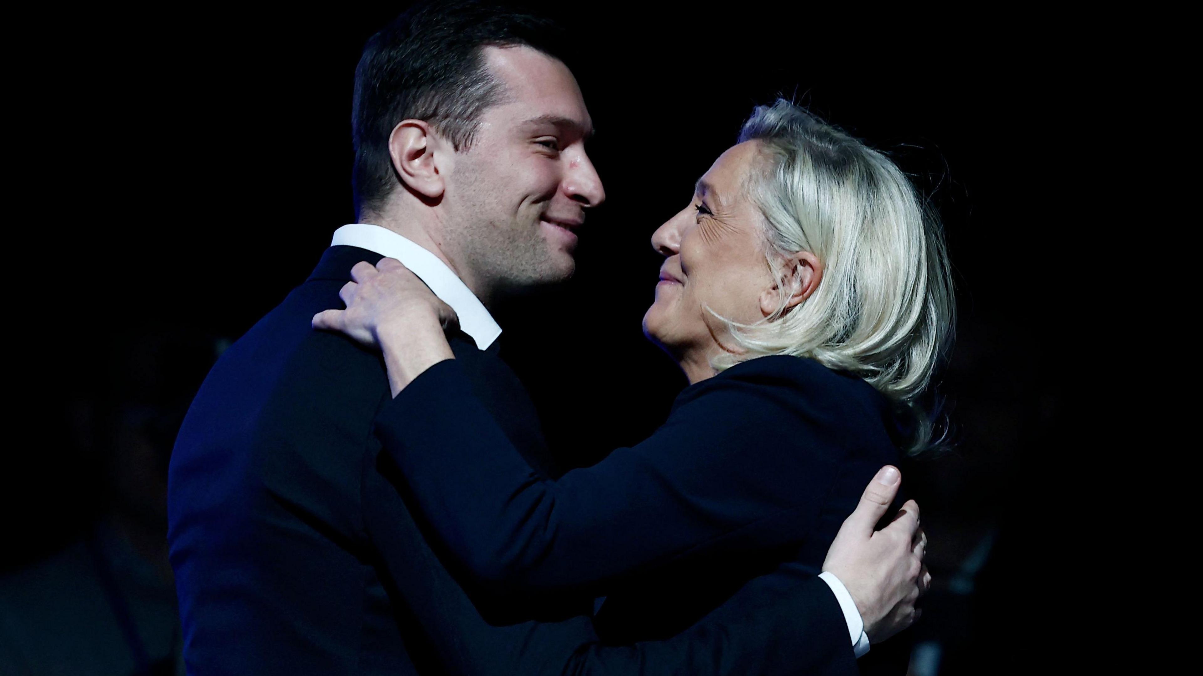 French far-right Rassemblement National RN party's President Jordan Bardella and the President of the party's parliamentary group Marine Le Pen greet each other during a party rally following the results of the first round of France's 2026 municipal elections, in Chalons-en-Champagne. They are smiling and embracing.