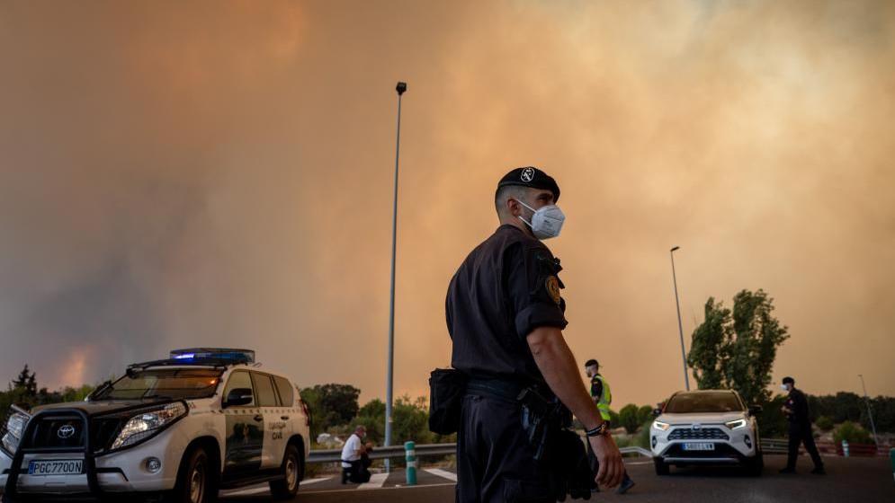 A Civil Guard officer wears a protective mask as smoke from a wildfire obscures the sky in Cenicientos, Madrid, Spain.