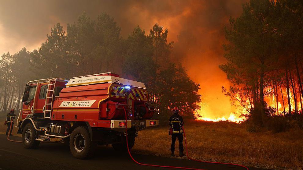 French firefighters try to extinguishing fires burning trees using a wildland water truck. The flames can be seen in the forested area