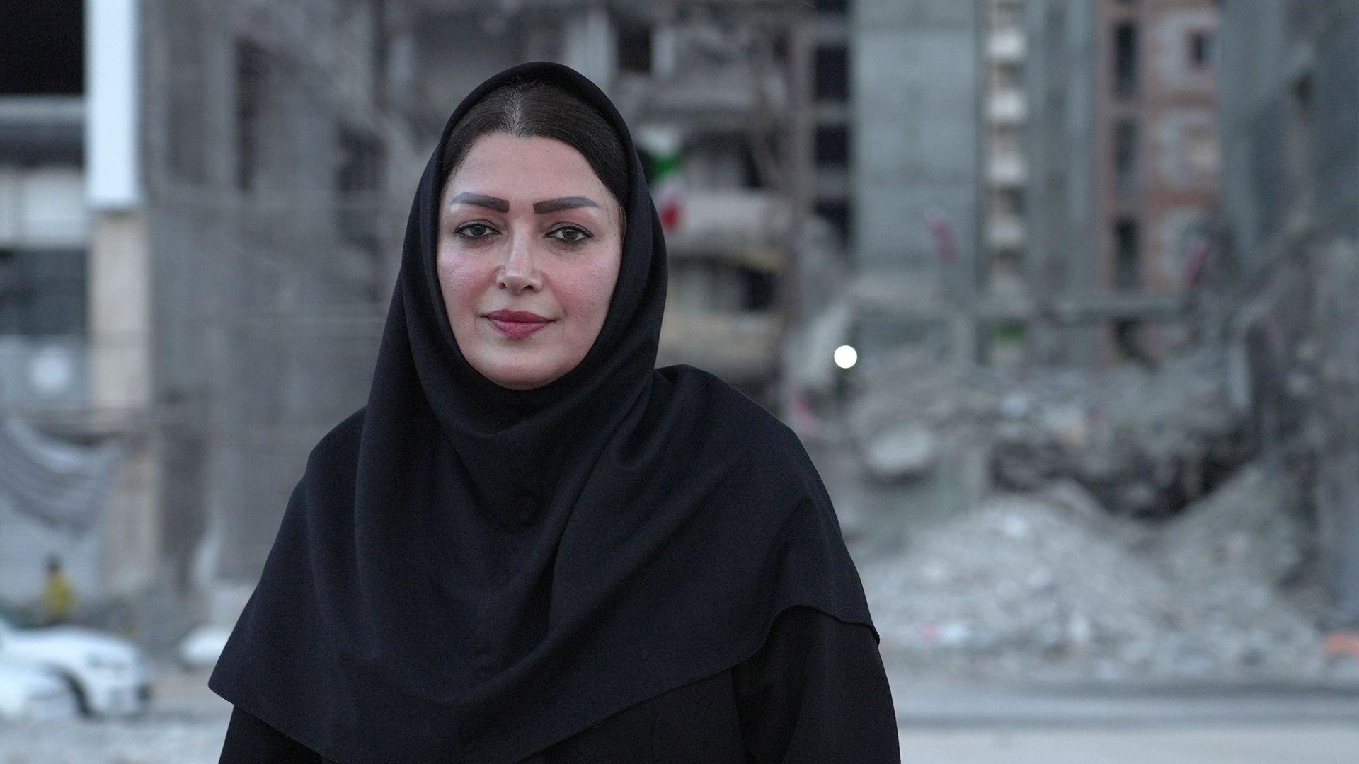 A woman looks directly at the camera. She is wearing black clothes including a headscarf.