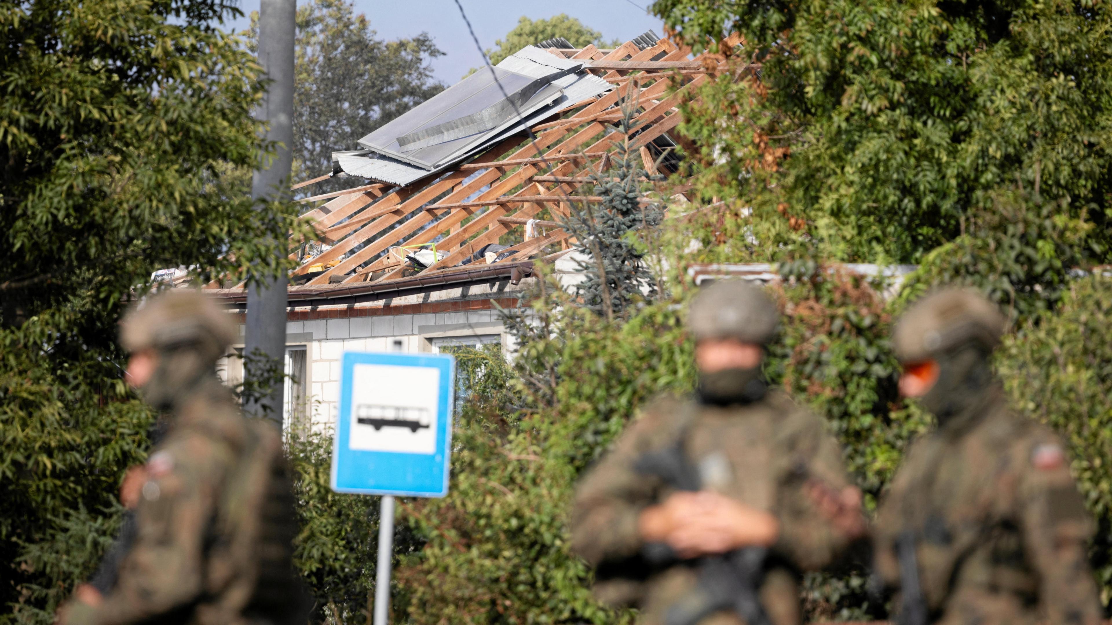Polish soldiers stand in front of a house destroyed with blown out roof