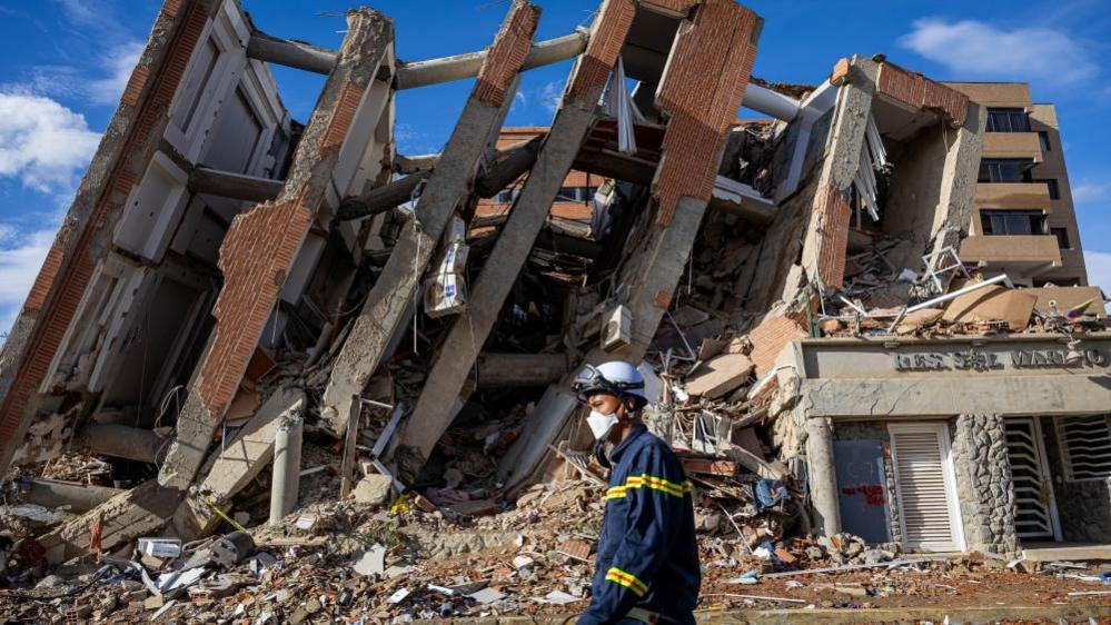 A rescuer walking past the rubble of destroyed buildings in La Guaira