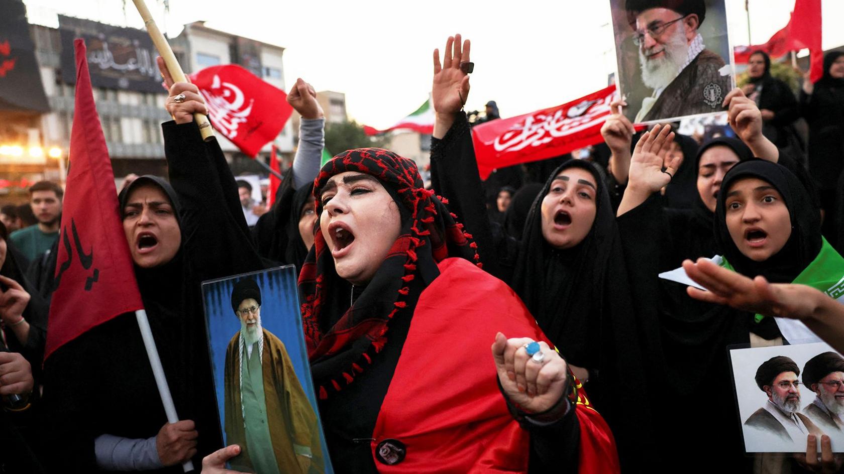 Mourners shout slogans on the day of a funeral procession for Iran's late Supreme Leader Ayatollah Ali Khamenei. In shot is a group of women holding photos of Khamenei. The lady in the centre is wearing red and black and shouting