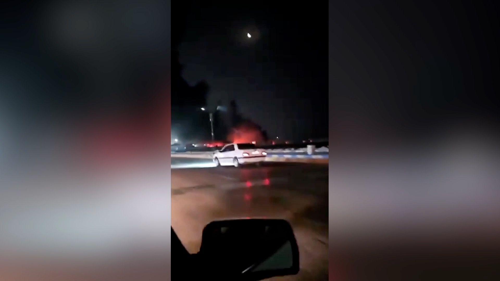 Fire in the distance as cars drive on the road.
