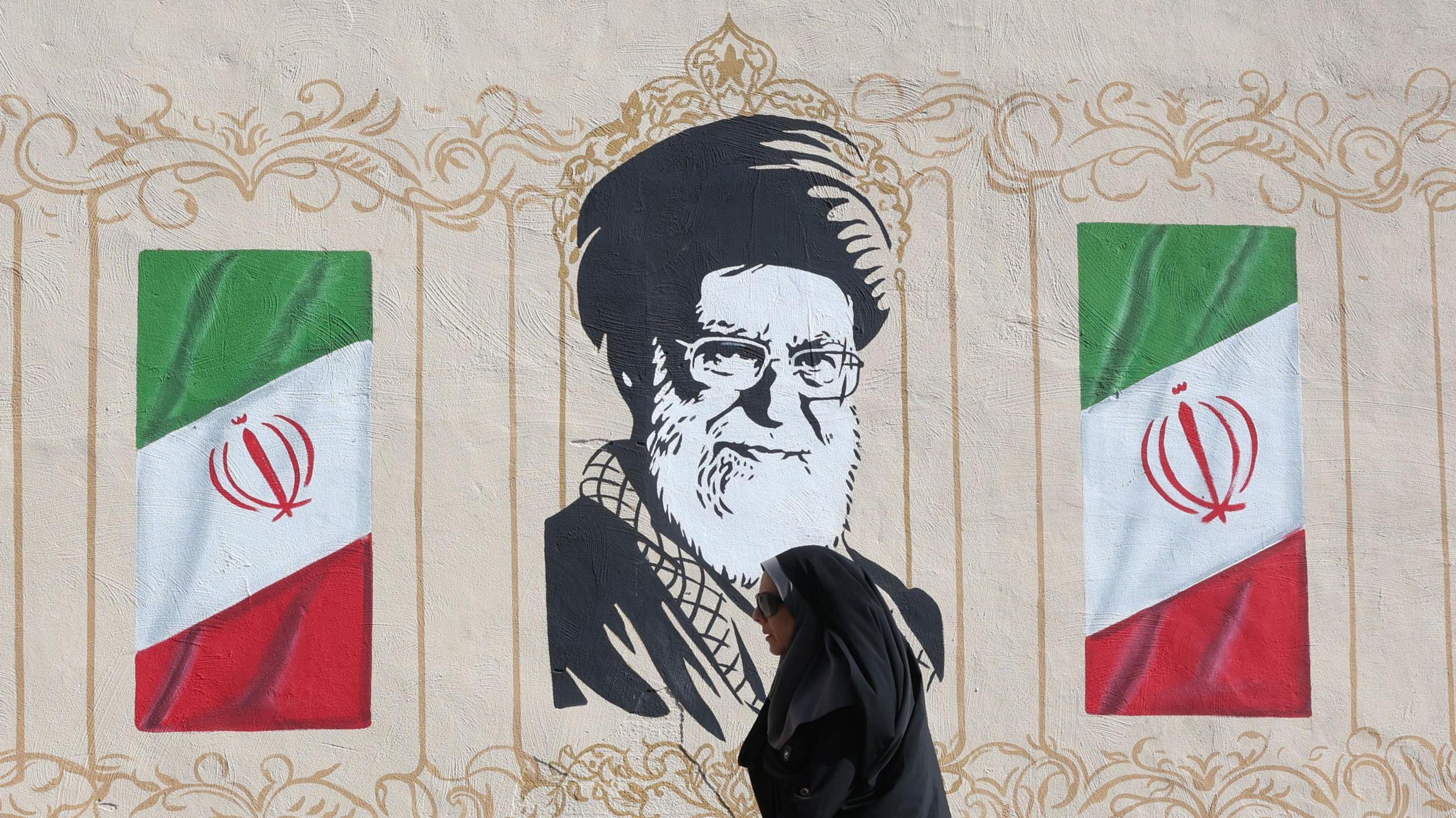 An Iranian woman walks past a mural of on a street in Tehran, Iran, 15 July 2026.