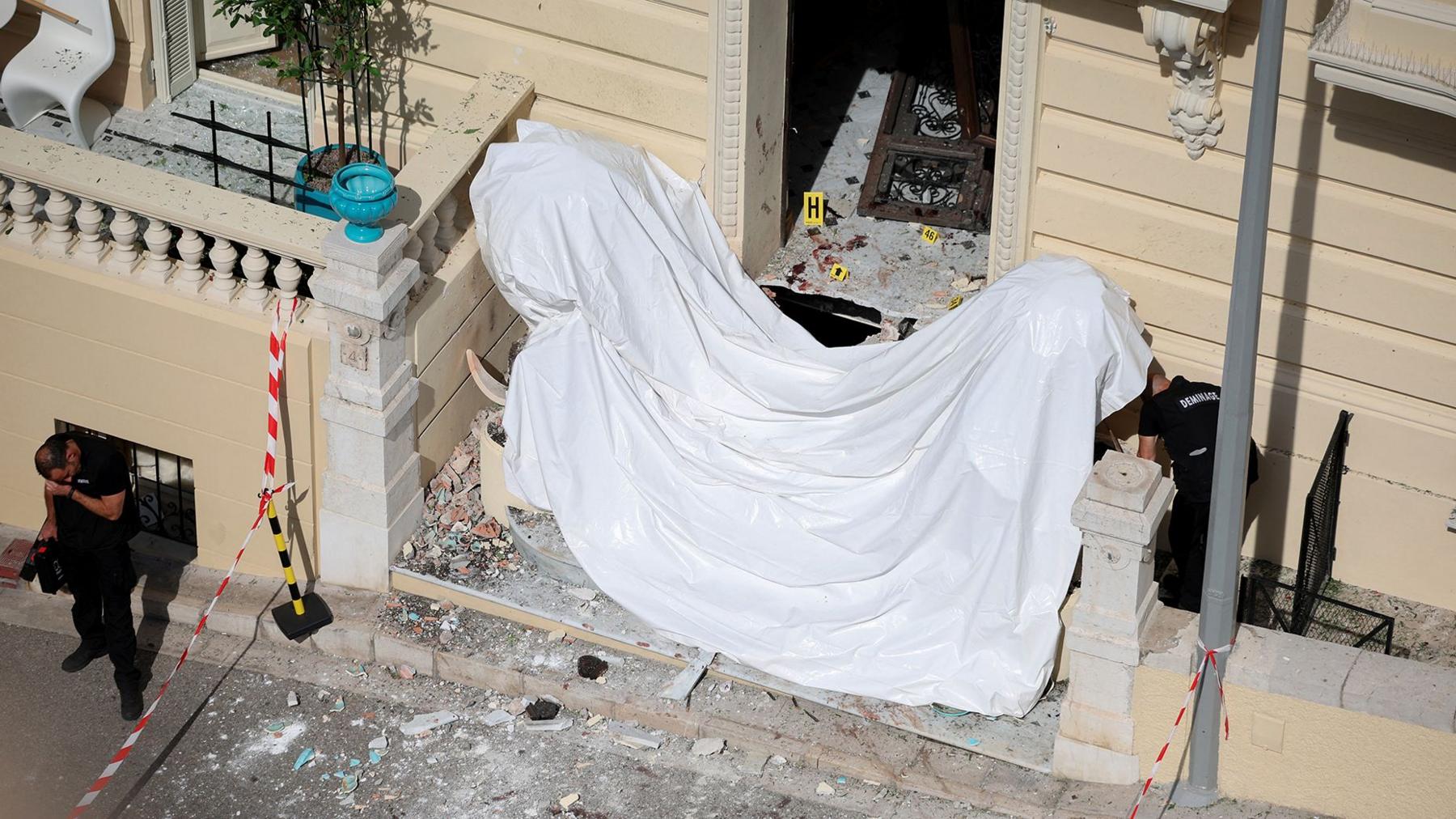 Frontage of a large cream coloured residential building in Monaco with damage to windows and a white sheet across the front steps and police standing near the front of the building. Photo: 30 June 2026