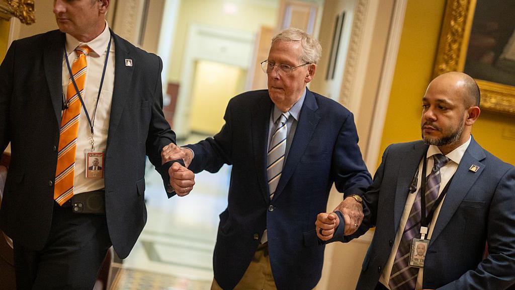 McConnell holding the hands of two men on either side of him for support