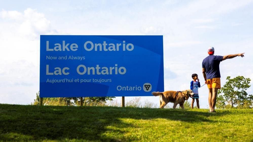 A family walks by a sign reading "Lake Ontario, Now and Always," unveiled by Ontario Premier Doug Ford at Fifty Point Conservation Area, near Grimsby, Ontario, Canada.