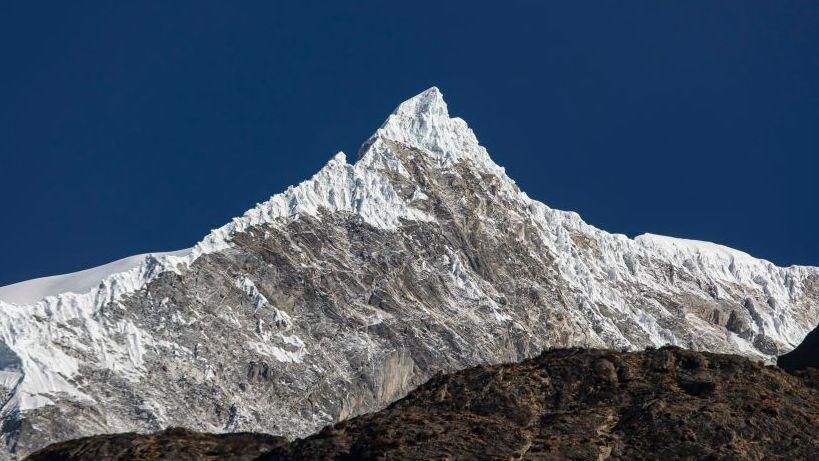 A panomanic view of the Langtang Lirung peak. The snowy summit is seen against a clear blue sky.