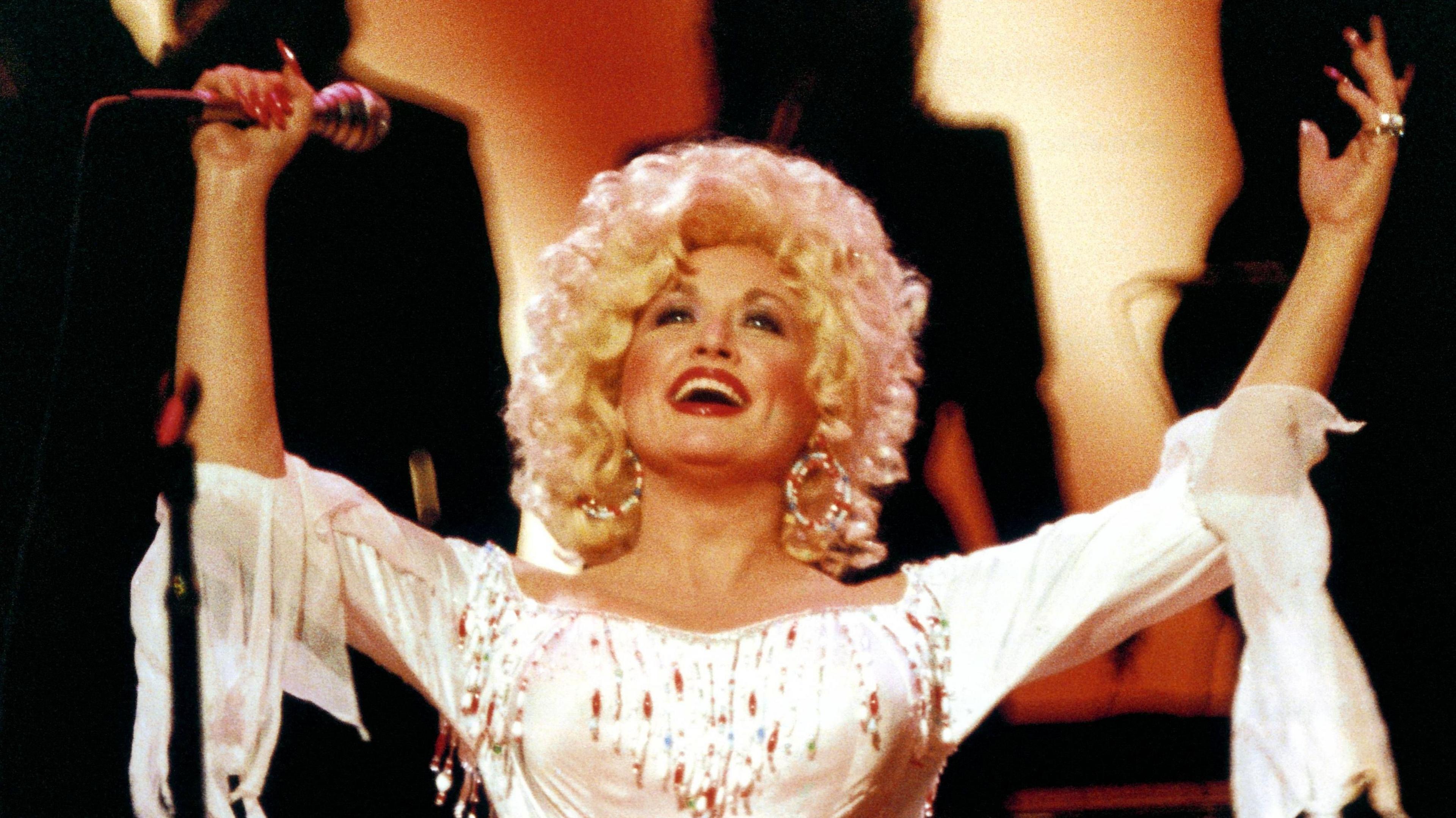 Dolly Parton with both arms raised on stage in 1983