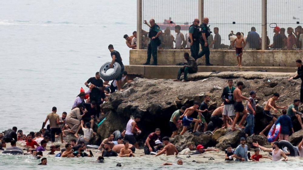 Several migrants attempt to enter Cueta via the sea, three police officers walk by a fence
