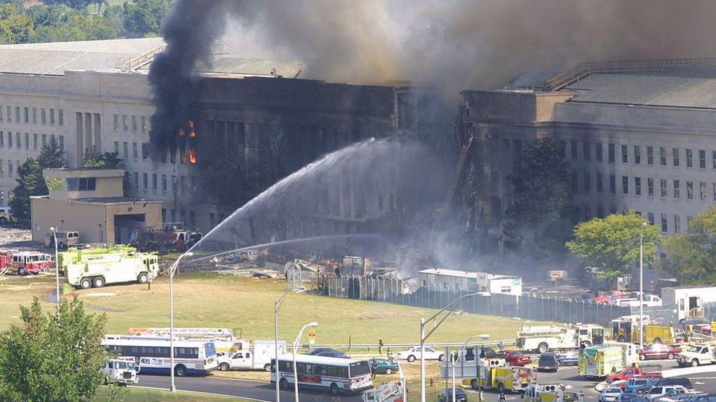 Smoke comes out from the west wing of the Pentagon on 11 September 2001 while fire engines spray water into the buildings.
