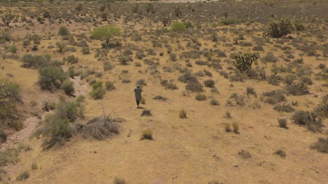 Holly Ratchford walks in the desert near where she now lives. There are mountains in the background.