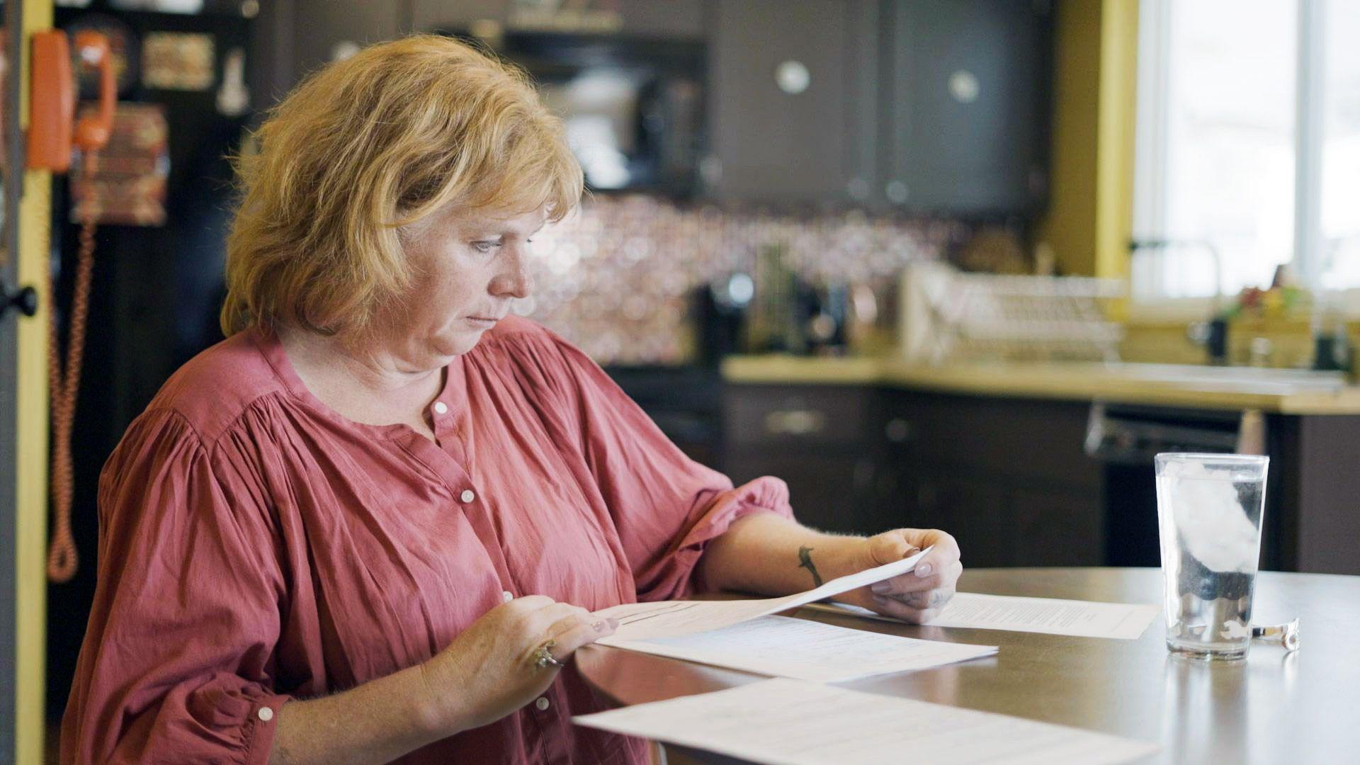 Holly Ratchford, who wears a pink blouse, looks through documents in her kitchen.