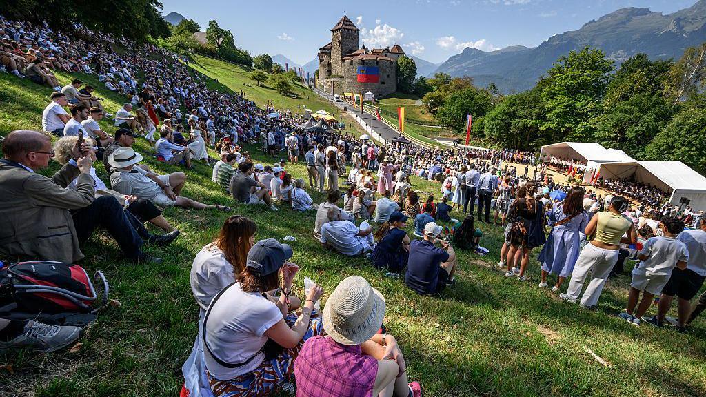 Hundreds of people gather on the slopes below Vaduz Castle, the palace and official residence of the Prince of Liechtenstein, during its National Day celebrations in Vaduz, on 15 August. Mountains can be seen in the background.