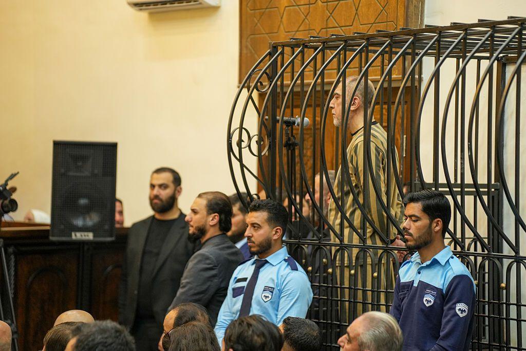 Ateb Najib stands inside a cage wearing a striped uniform as he is sentenced in a courtroom in Damascus, Syria.