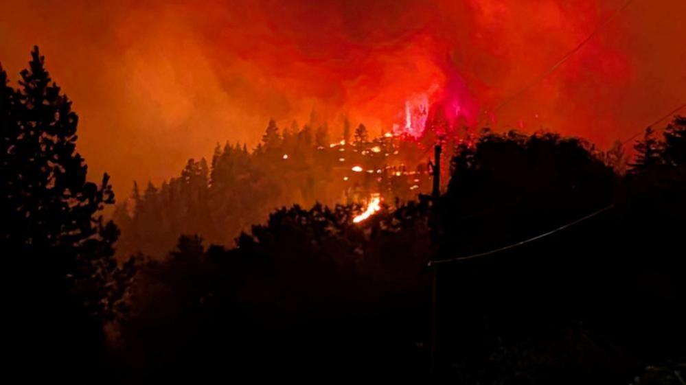Red flames and smoke rising in night sky from hilly forest