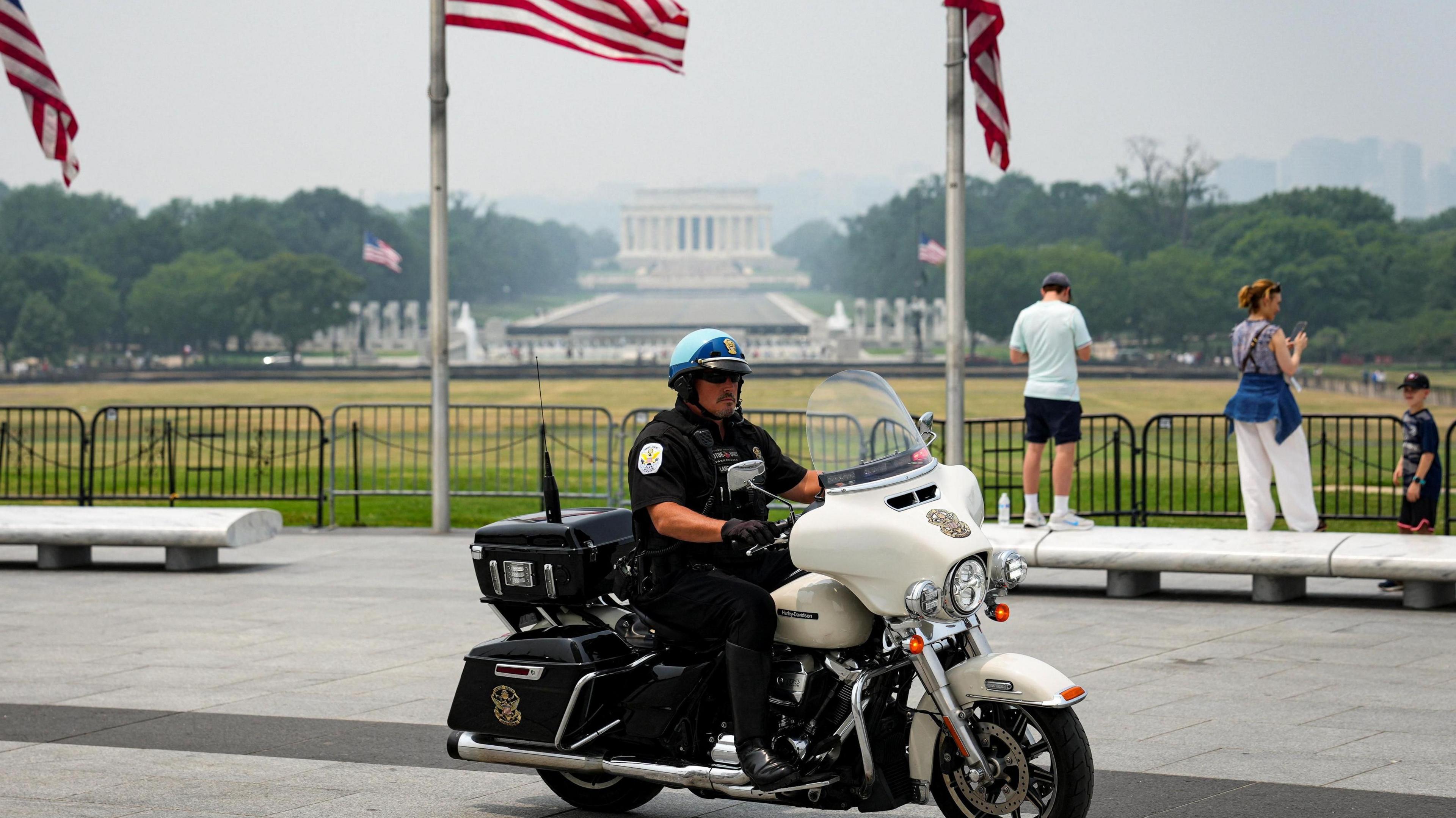 A US Park Police officer sits on a motorbike in front of the Washington Monument, with American flags in the background