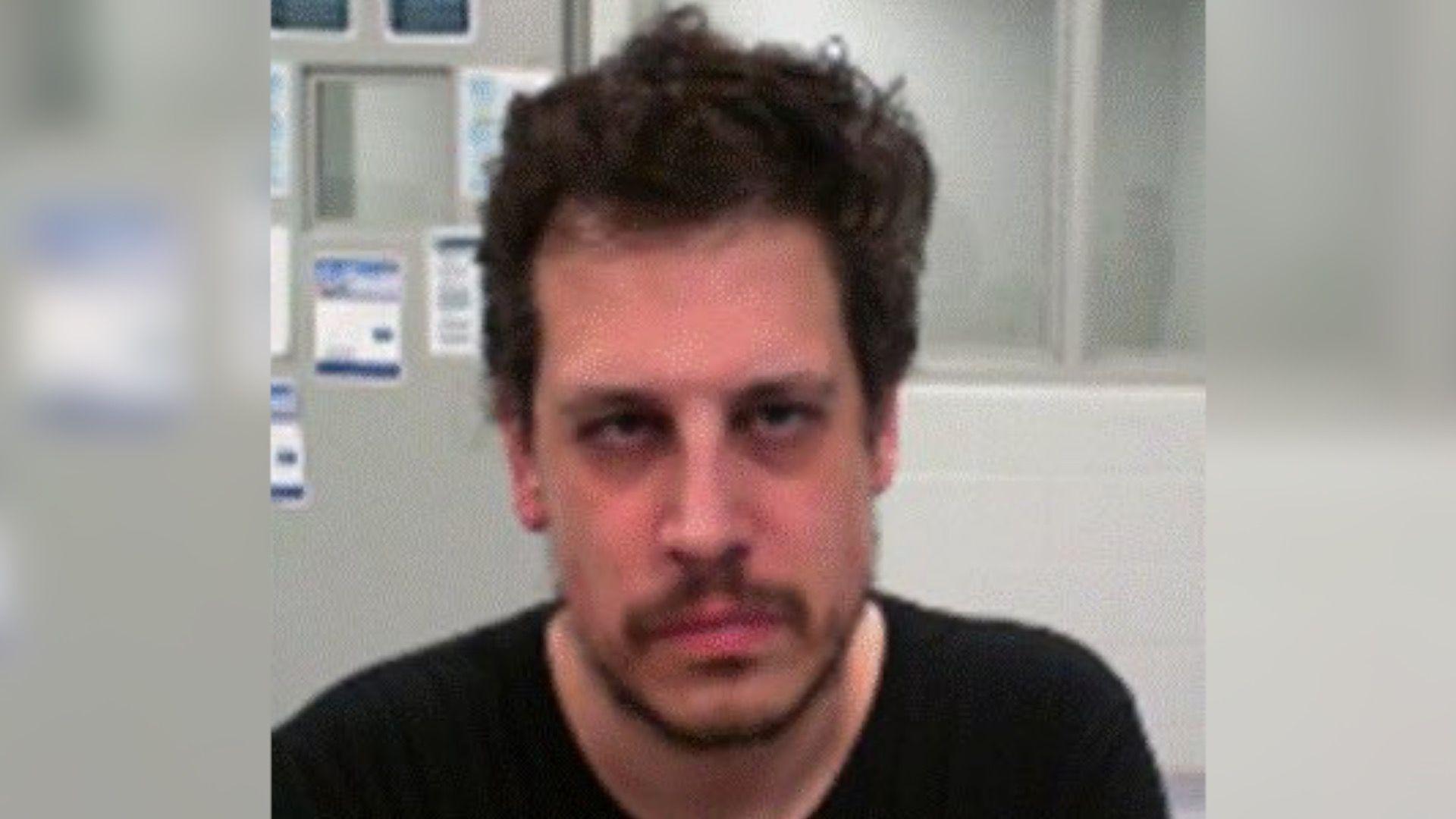 DHS released an mugshot of Yiannopoulos after his arrest. He wears a black shirt and has facial hair