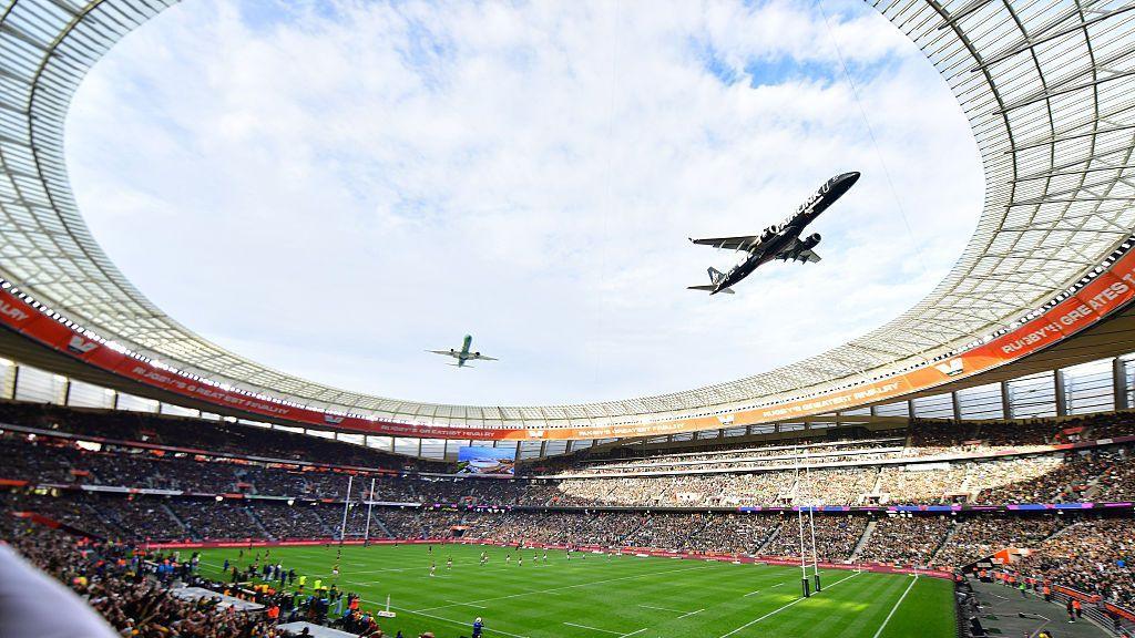 A fish-eye view from the stands of a rugby stadium looking up at the sky as two planes fly in close formation above.