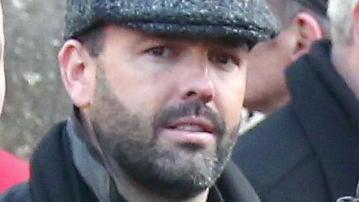 Daniel Kinahan, a man with short dark hair and a stubbly beard, pictured at a funeral in 2016. He is wearing a grey peaked cap, a black shirt and a black coat with the collar pulled up.