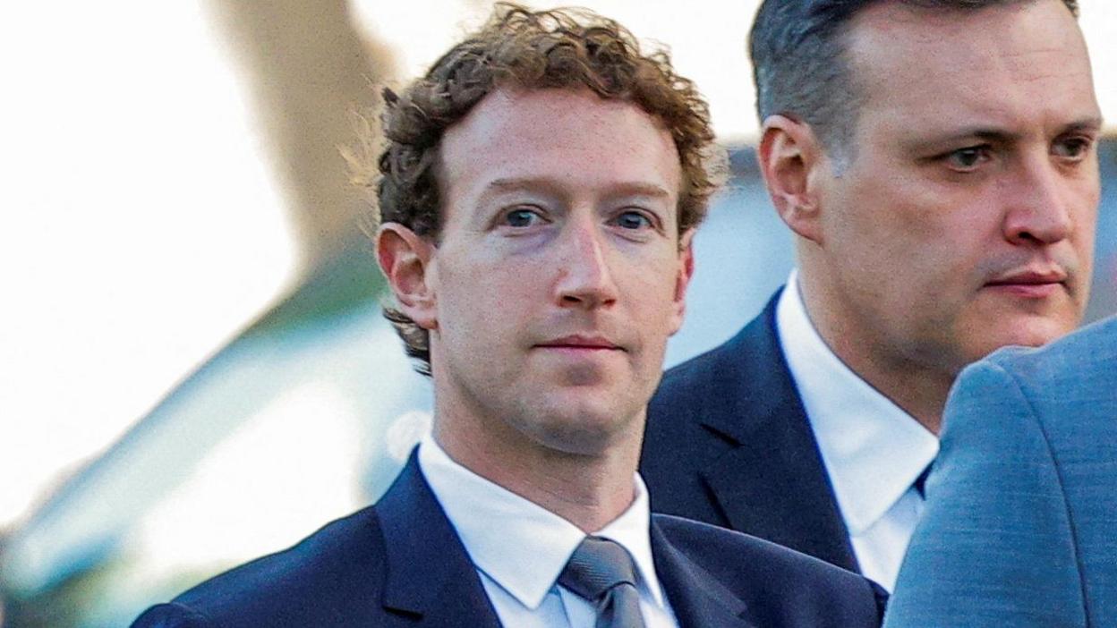 Close up of Mark Zuckerberg wearing a suit, looks towards the camera with a blank expression. He is flanked by staff also in suits. Photographed in February 2026