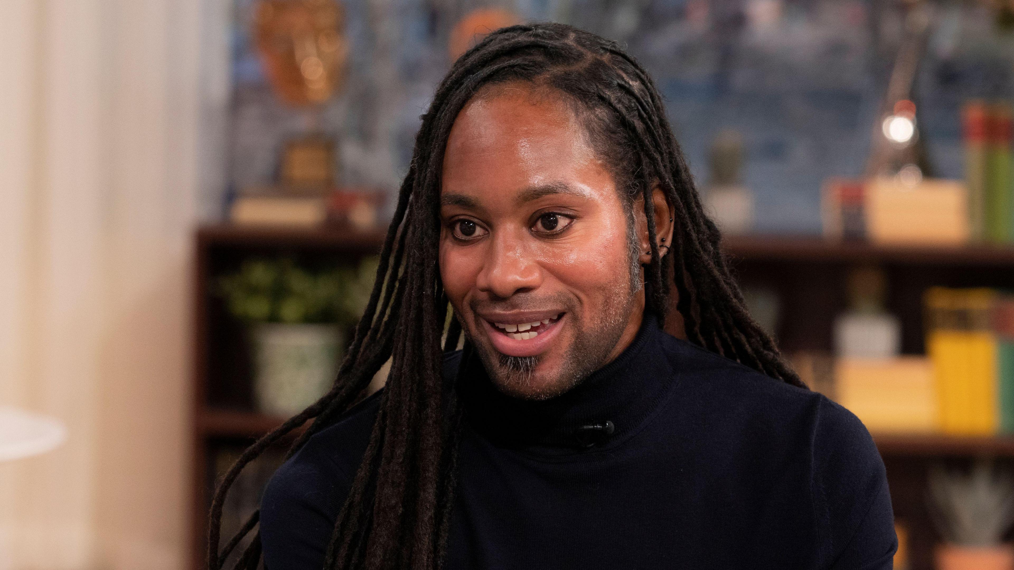 Jason Arday pictured during a TV interview in March 2023. He wears a black turtle-neck top.