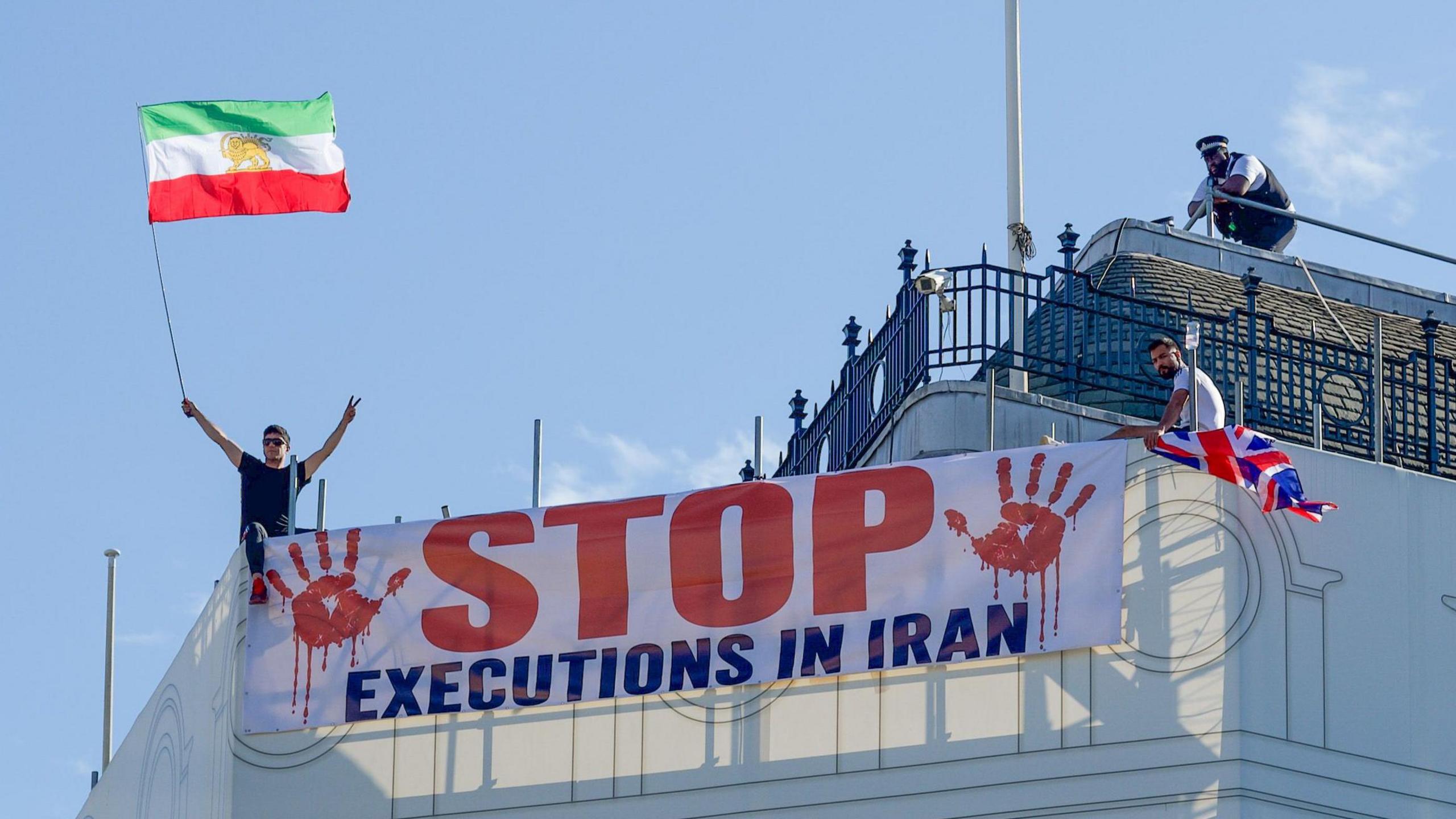 Protesters hold a banner saying "stop executions in Iran" and wave an Iranian flag during a demonstration on the roof of the Trocadero, overlooking Piccadilly Circus, central London (30 July 2026)