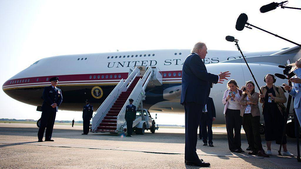 Trump stands in front of Qatari-gifted Air Force One and speaks to reporters who are holding boom microphones