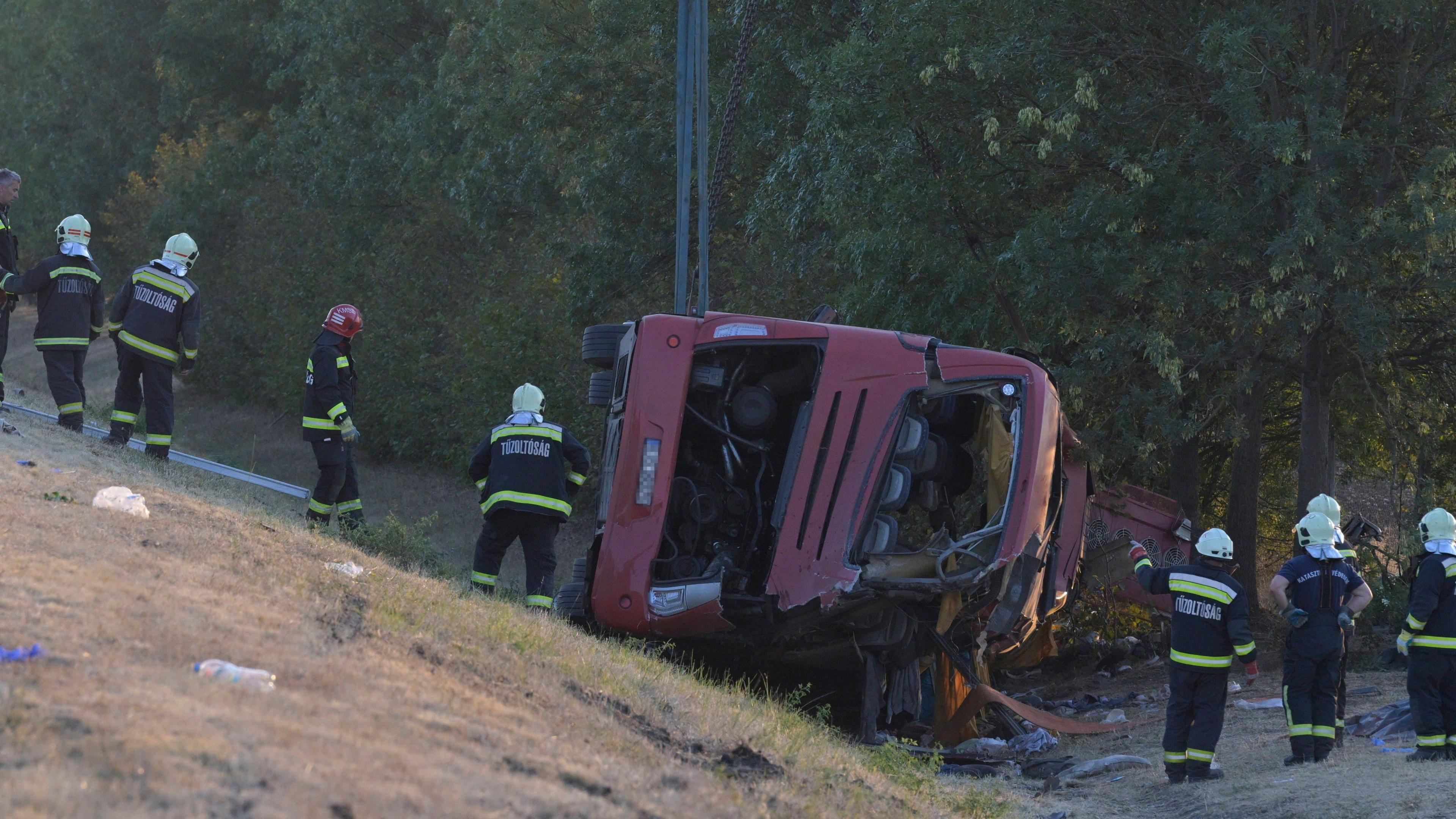 A crumpled red bus sits at the bottom of a ravine as firefighters attend.