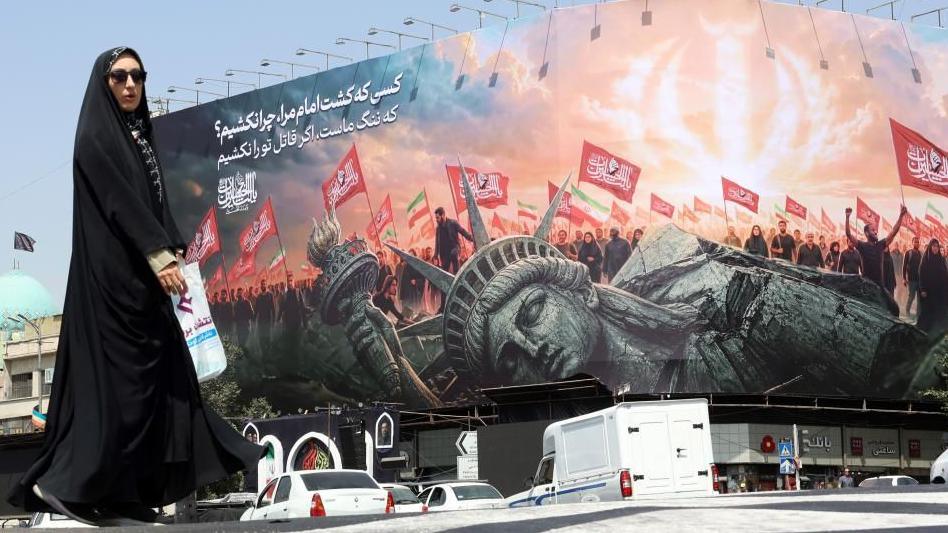 A veiled Iranian woman walks past an anti-US billboard at Enghelab Square in central Tehran
