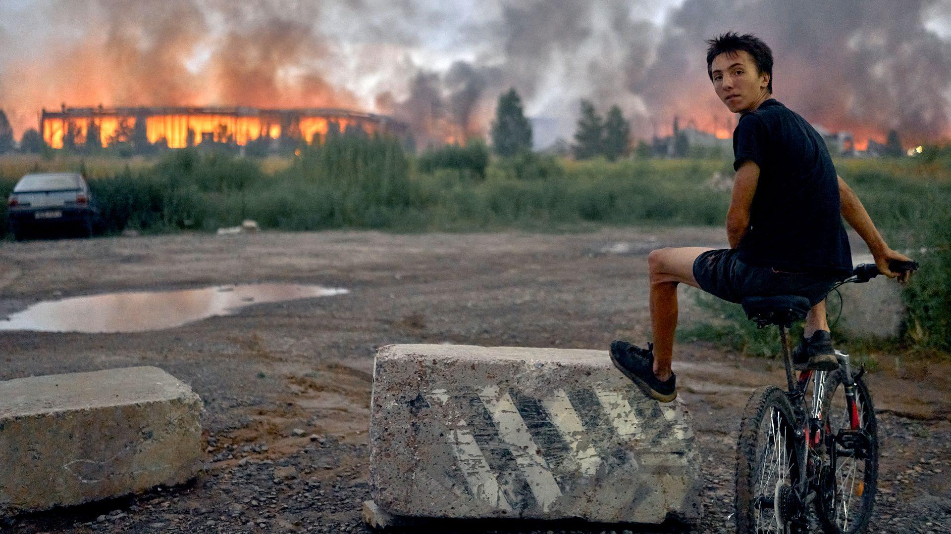 A teenager sits on a bicycle watching flames rise from a burning logistics warehouse following a Russian ballistic missile attack on Kyiv and the surrounding region on August 5, 2026 in Kyiv, Ukraine.