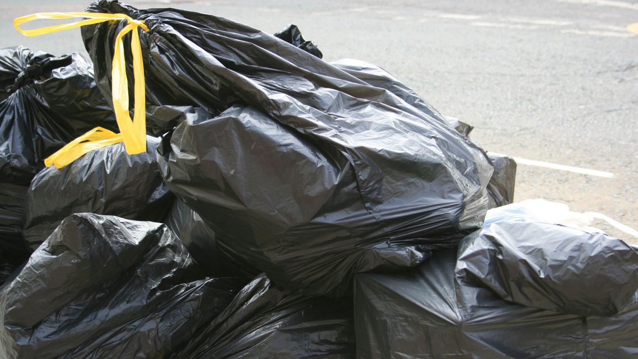 Black bin bags with yellow handles stacked on top of each other